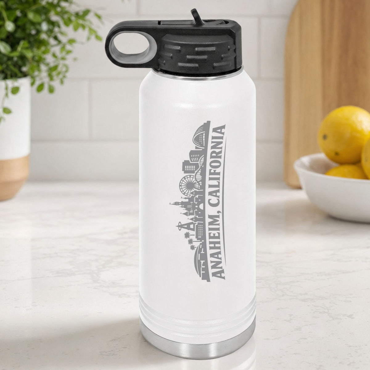 White 32 oz insulated water bottle laser engraved with the Anaheim, California skyline running up the side, standing on a kitchen counter