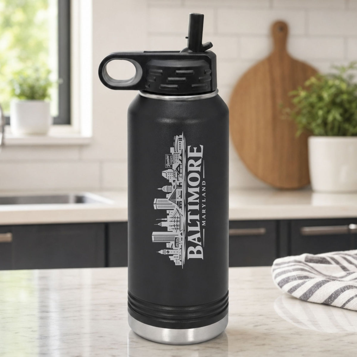 Black 32 oz insulated water bottle laser engraved with the Baltimore, Maryland skyline running up the side, standing on a kitchen counter