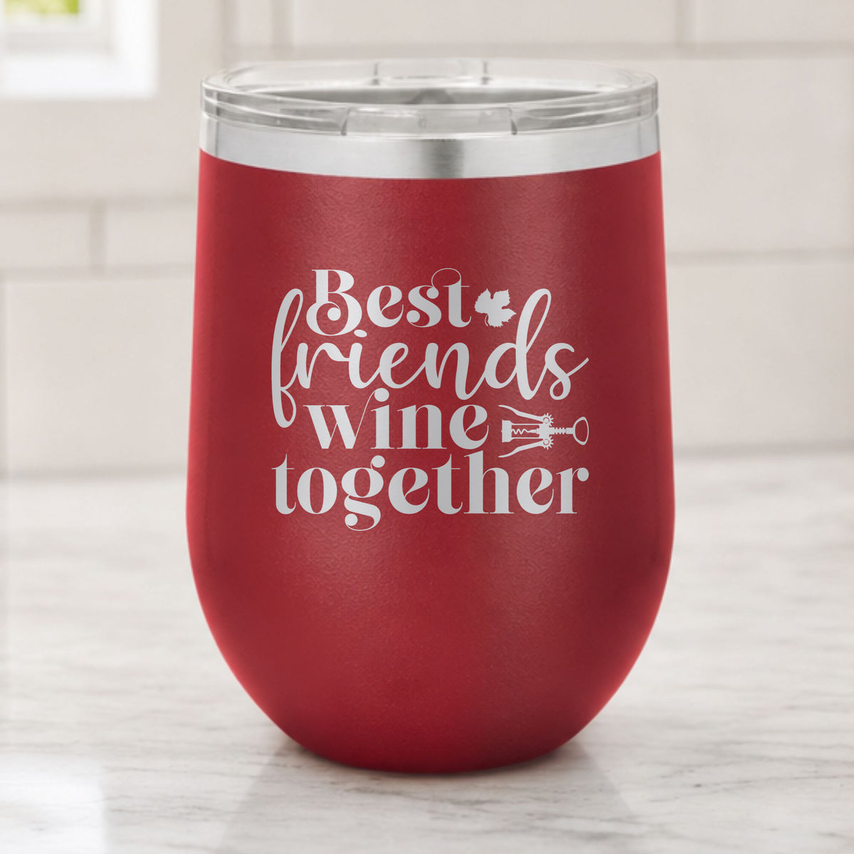 Maroon 12 oz stemless wine tumbler laser engraved with "Best Friends Wine Together", on a kitchen counter
