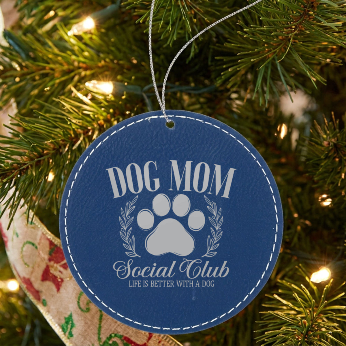 Blue leatherette Christmas ornament engraved with a Dog Mom Social Club crest design with a paw print and laurel wreath