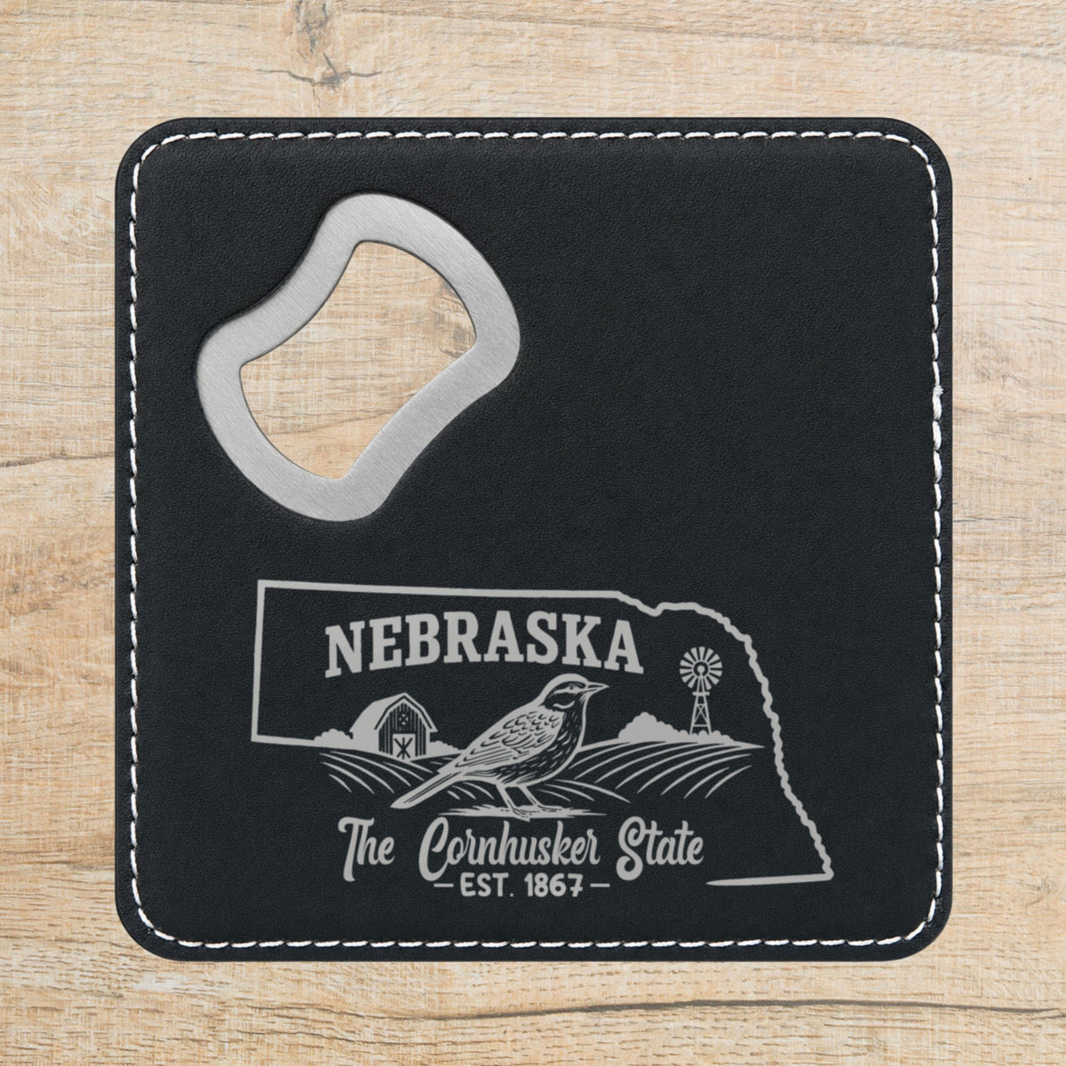 Black leatherette bottle opener coaster laser engraved with a Nebraska design of a western meadowlark, a barn and a windmill