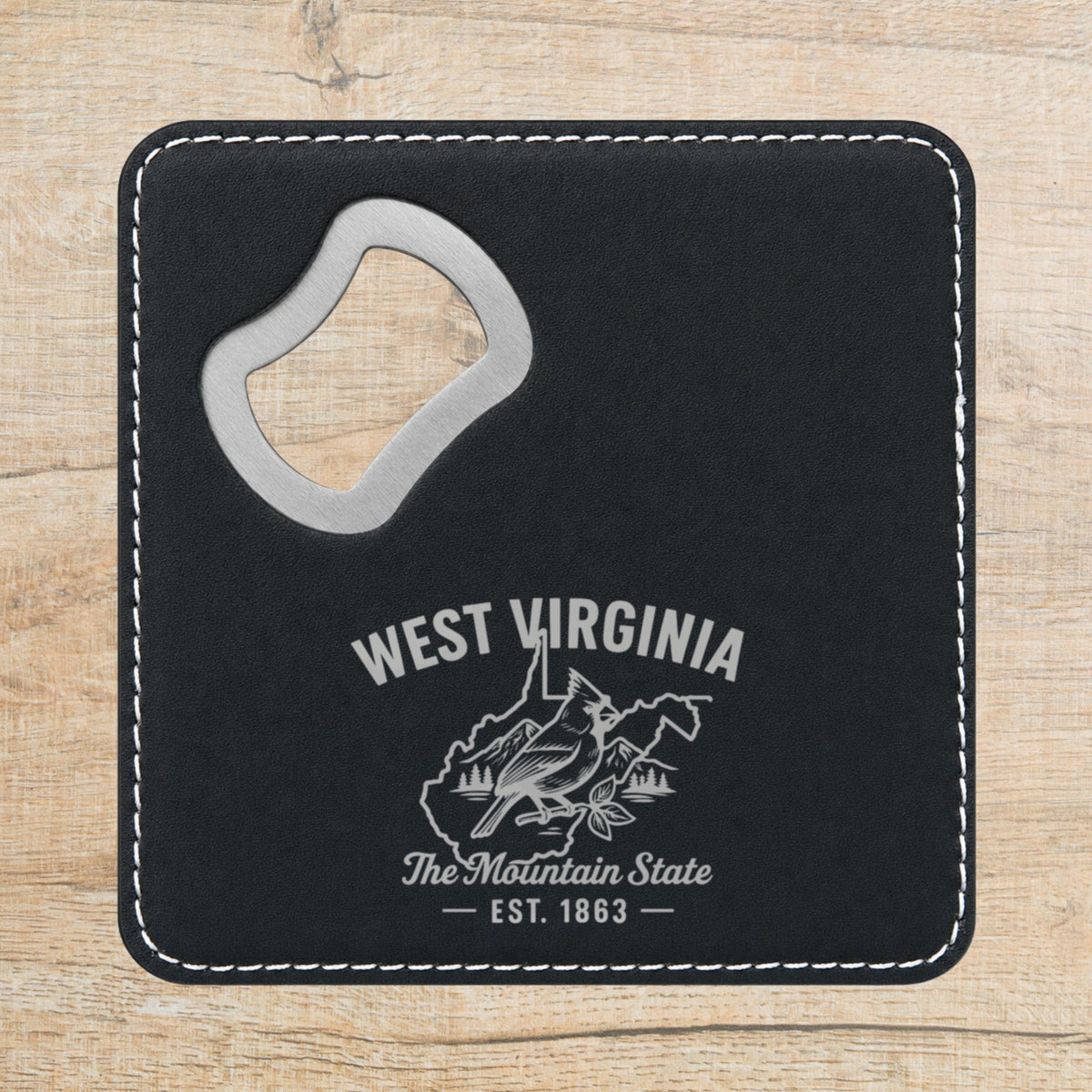 Black leatherette bottle opener coaster laser engraved with a West Virginia design of a cardinal, mountains and pines