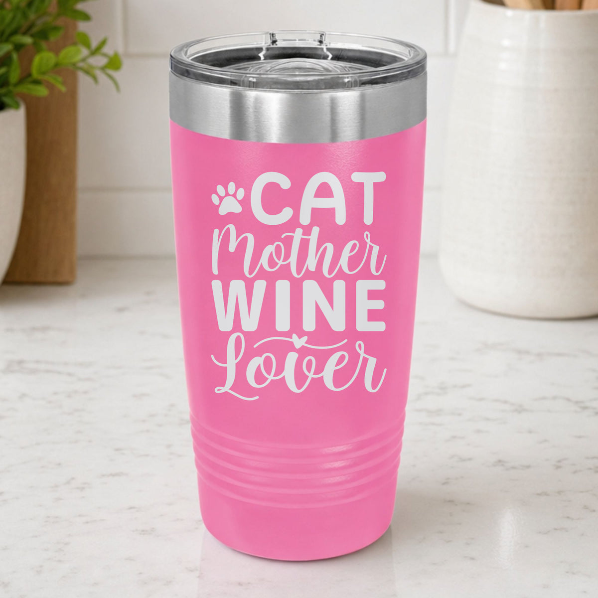 Pink 20 oz tumbler laser engraved with "Cat Mother Wine Lover" and a paw print, on a kitchen counter