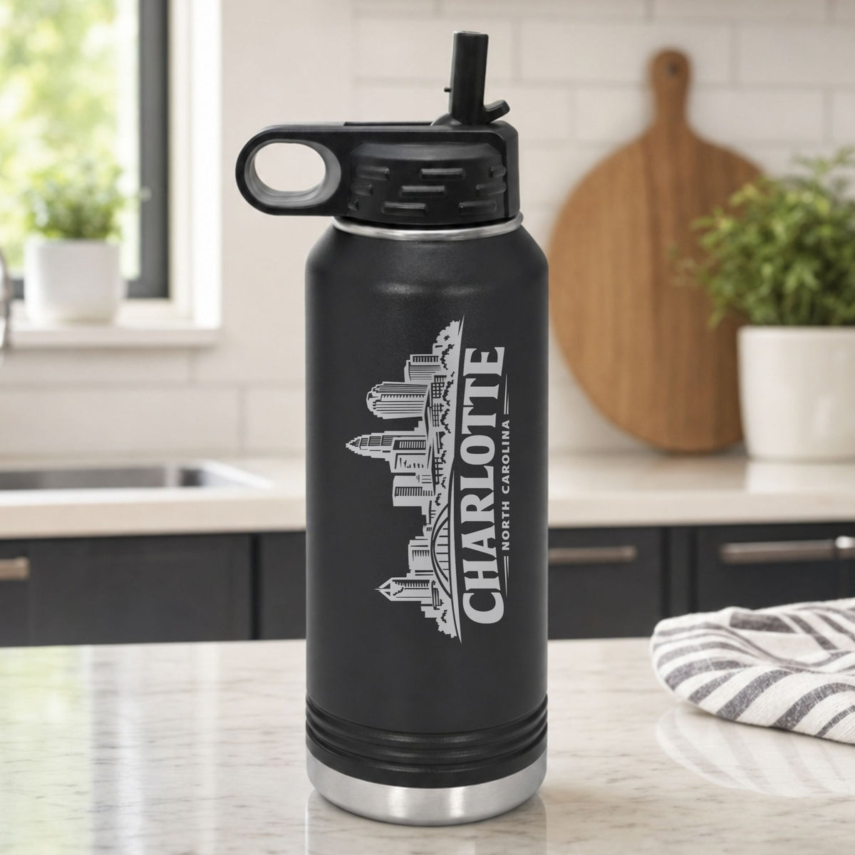 Black 32 oz insulated water bottle laser engraved with the Charlotte, North Carolina skyline running up the side, standing on a kitchen counter