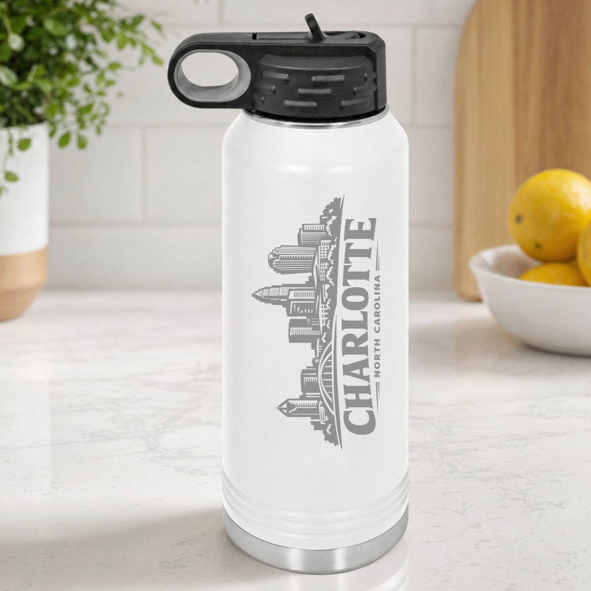 White 32 oz insulated water bottle laser engraved with the Charlotte, North Carolina skyline running up the side, standing on a kitchen counter