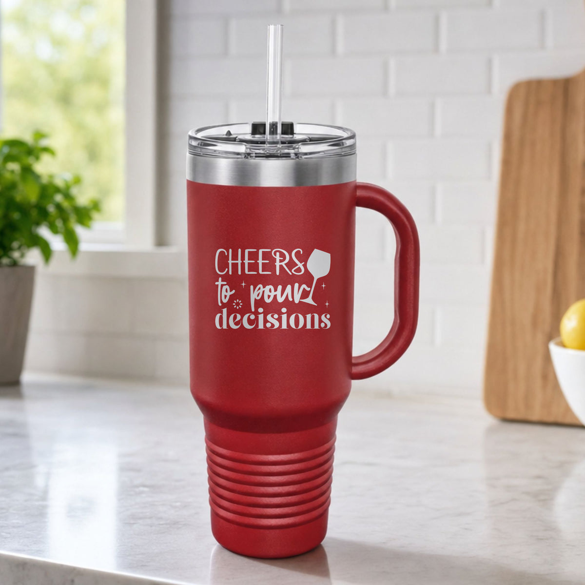 Maroon 40 oz tumbler with handle and straw laser engraved with "Cheers to Pour Decisions", on a kitchen counter