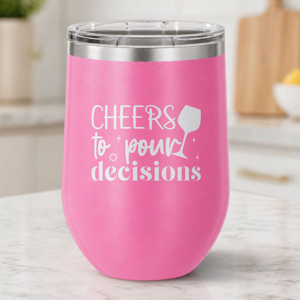 Pink 12 oz stemless wine tumbler laser engraved with "Cheers to Pour Decisions", on a kitchen counter