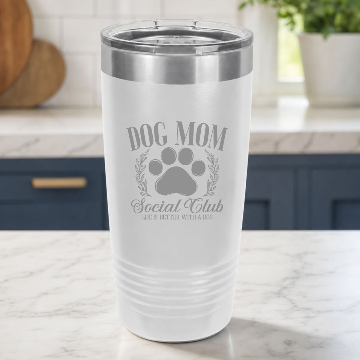 White 20 oz tumbler laser engraved with the Social Club "Dog Mom" design, on a kitchen counter