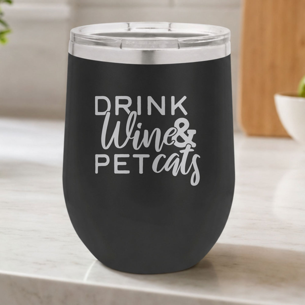 Black 12 oz stemless wine tumbler laser engraved with "Drink Wine & Pet Cats", on a kitchen counter
