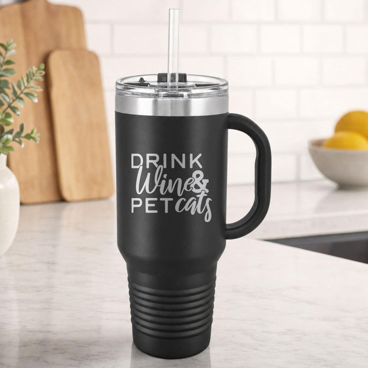 Black 40 oz tumbler with handle and straw laser engraved with "Drink Wine & Pet Cats", on a kitchen counter