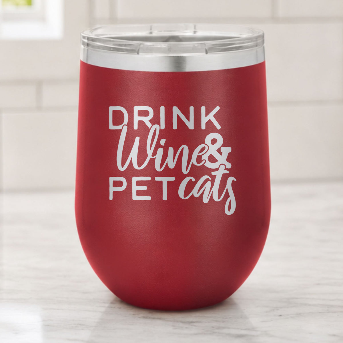 Maroon 12 oz stemless wine tumbler laser engraved with "Drink Wine & Pet Cats", on a kitchen counter