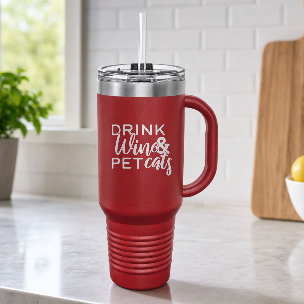 Maroon 40 oz tumbler with handle and straw laser engraved with "Drink Wine & Pet Cats", on a kitchen counter