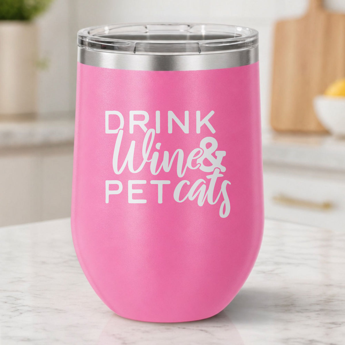 Pink 12 oz stemless wine tumbler laser engraved with "Drink Wine & Pet Cats", on a kitchen counter
