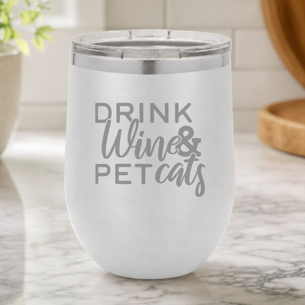 White 12 oz stemless wine tumbler laser engraved with "Drink Wine & Pet Cats", on a kitchen counter