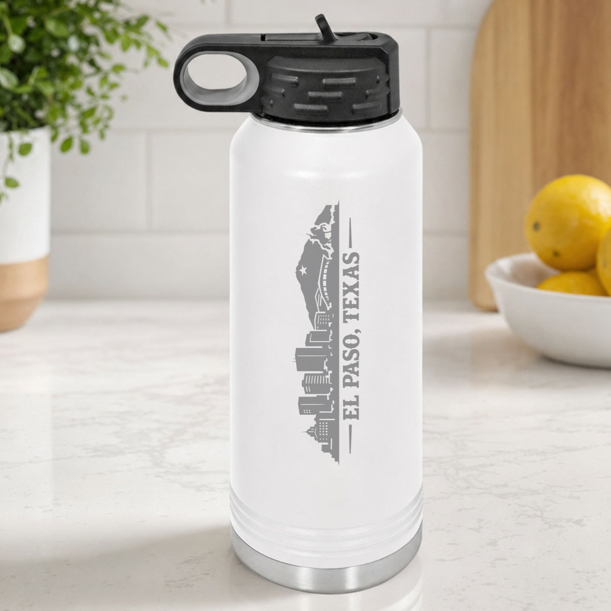 White 32 oz insulated water bottle laser engraved with the El Paso, Texas skyline running up the side, standing on a kitchen counter