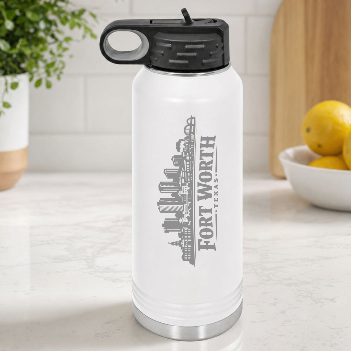 White 32 oz insulated water bottle laser engraved with the Fort Worth, Texas skyline running up the side, standing on a kitchen counter