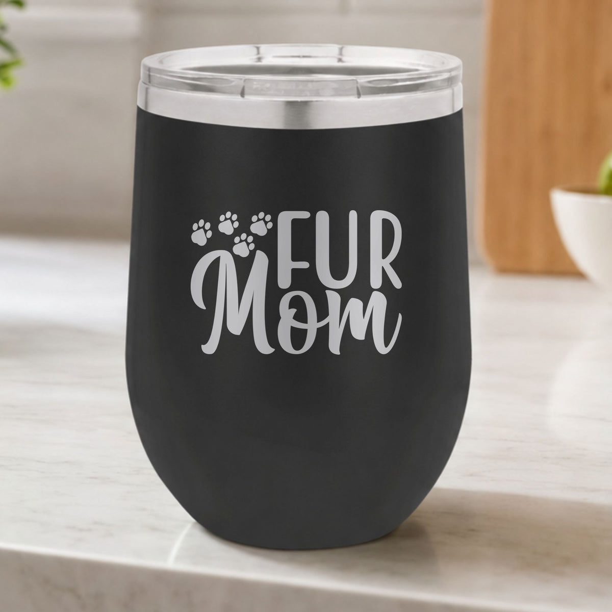 Black 12 oz stemless wine tumbler laser engraved with "Fur Mom", plus paw prints, on a kitchen counter