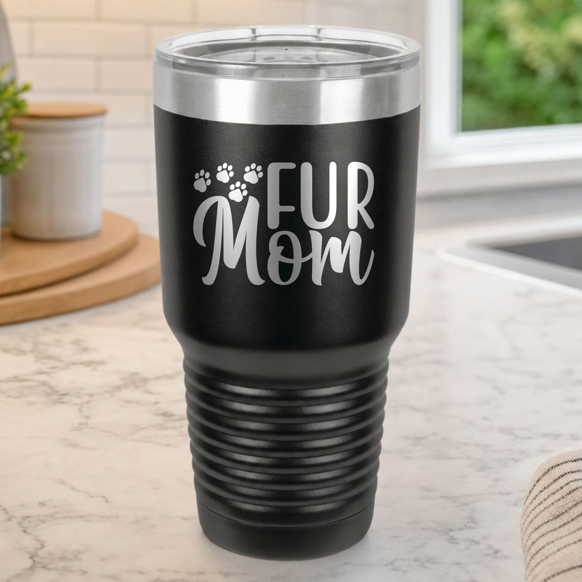 Black 30 oz tumbler laser engraved with "Fur Mom", plus paw prints, on a kitchen counter