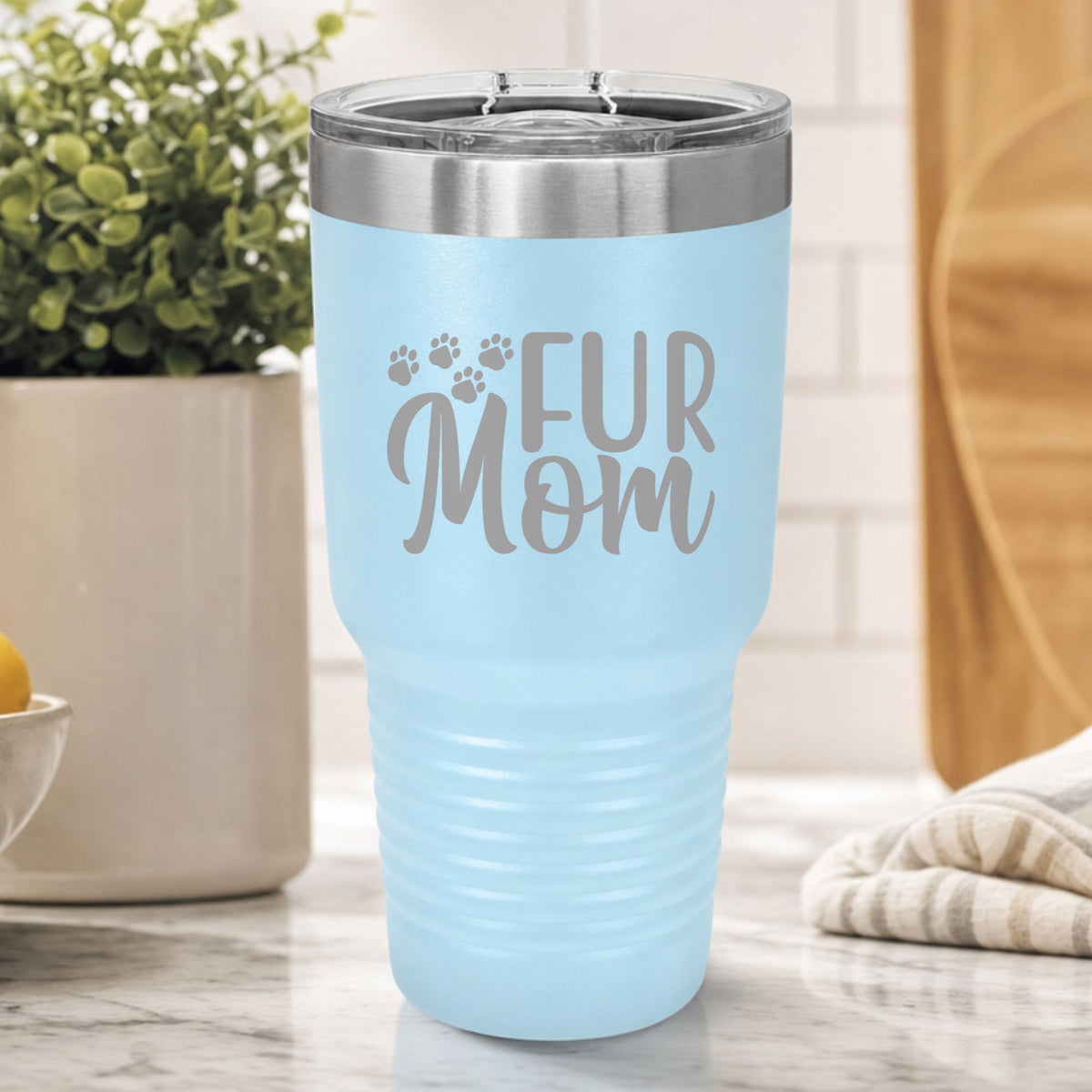 Light Blue 30 oz tumbler laser engraved with "Fur Mom", plus paw prints, on a kitchen counter