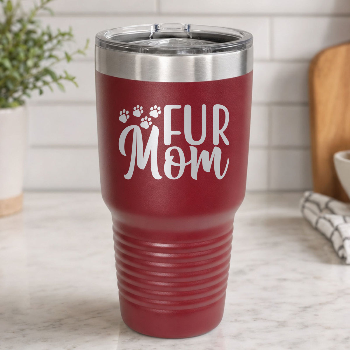 Maroon 30 oz tumbler laser engraved with "Fur Mom", plus paw prints, on a kitchen counter