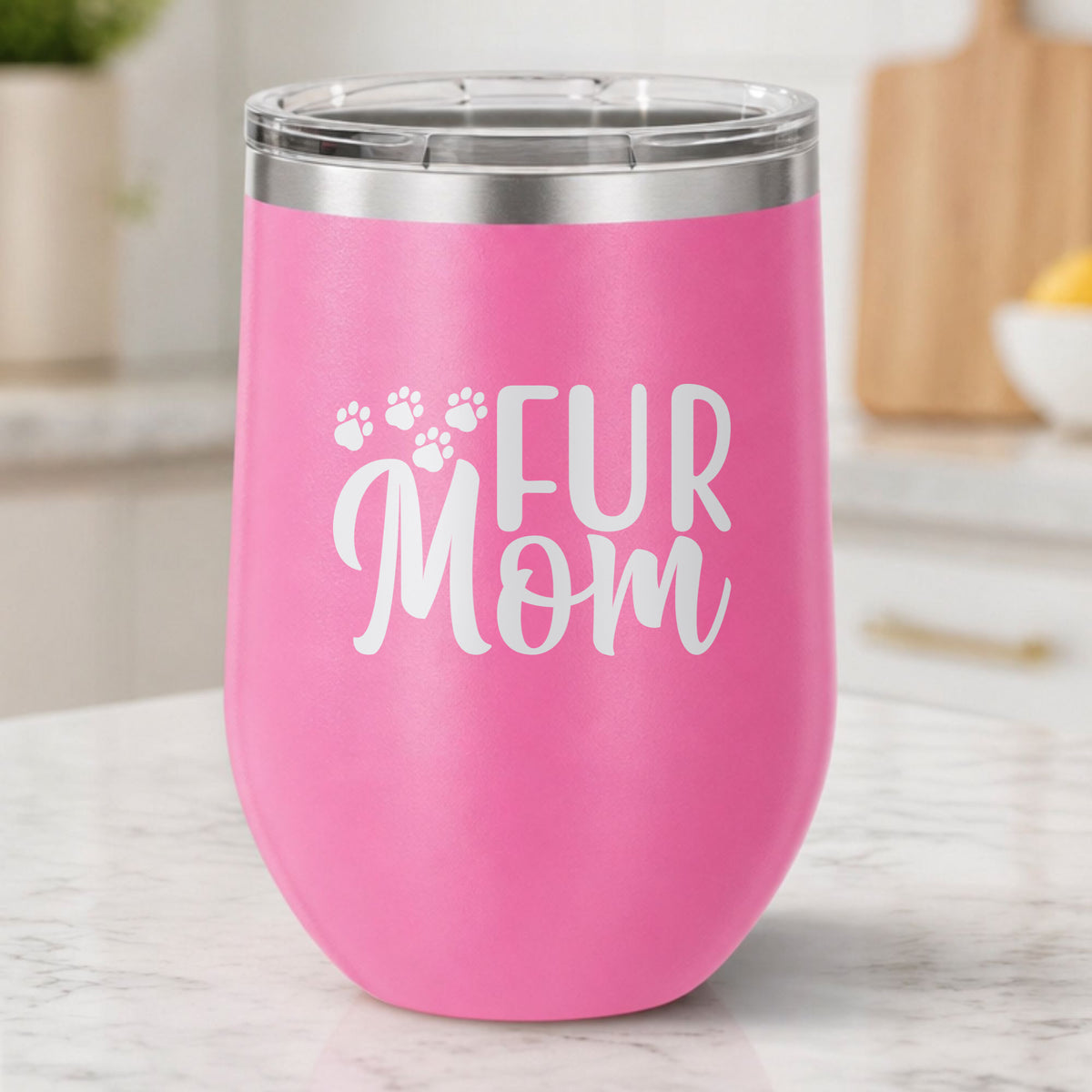 Pink 12 oz stemless wine tumbler laser engraved with "Fur Mom", plus paw prints, on a kitchen counter
