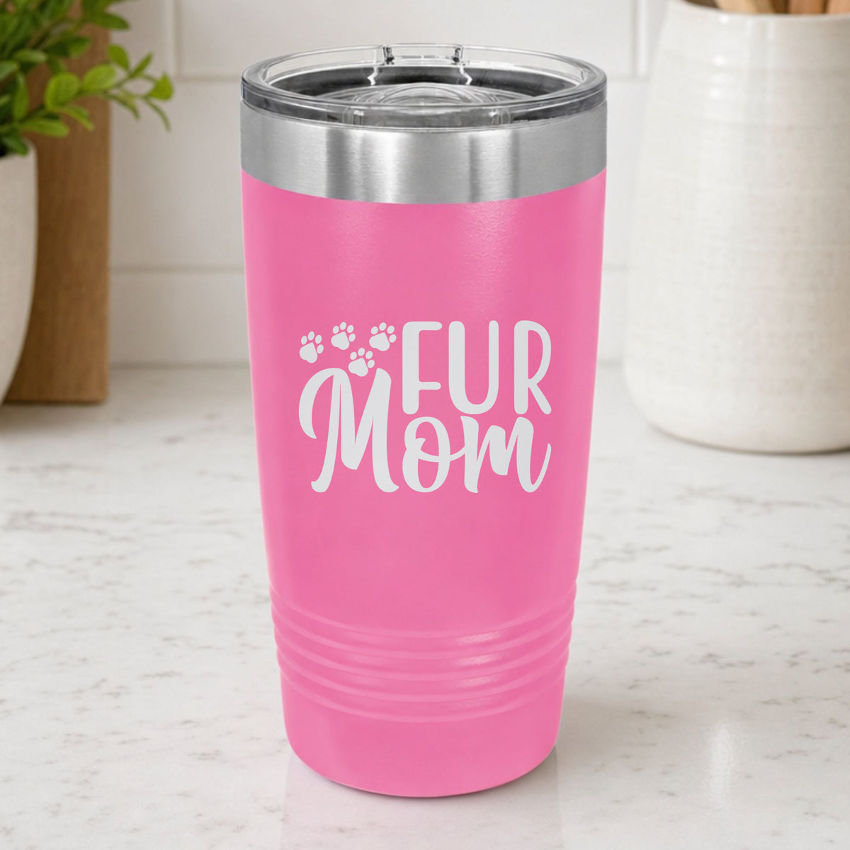 Pink 20 oz tumbler laser engraved with "Fur Mom", plus paw prints, on a kitchen counter