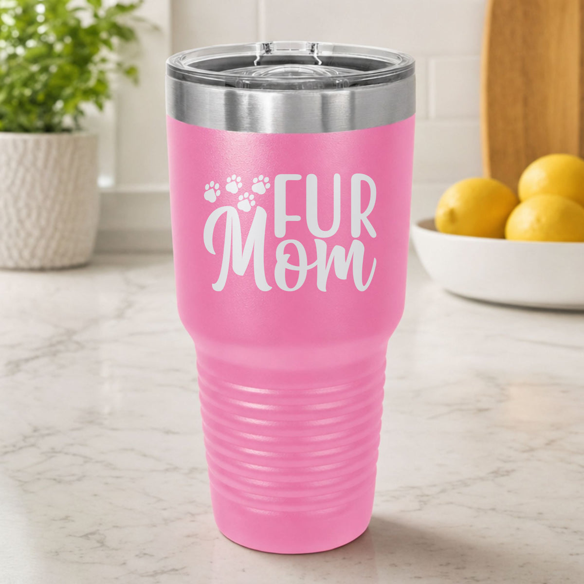 Pink 30 oz tumbler laser engraved with "Fur Mom", plus paw prints, on a kitchen counter