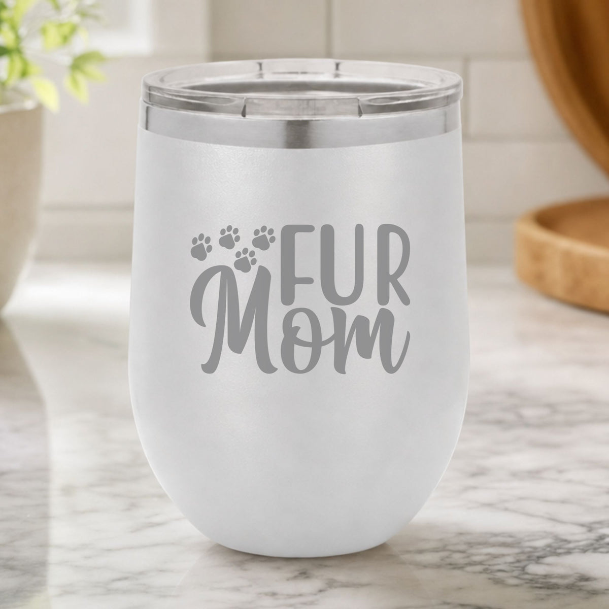 White 12 oz stemless wine tumbler laser engraved with "Fur Mom", plus paw prints, on a kitchen counter