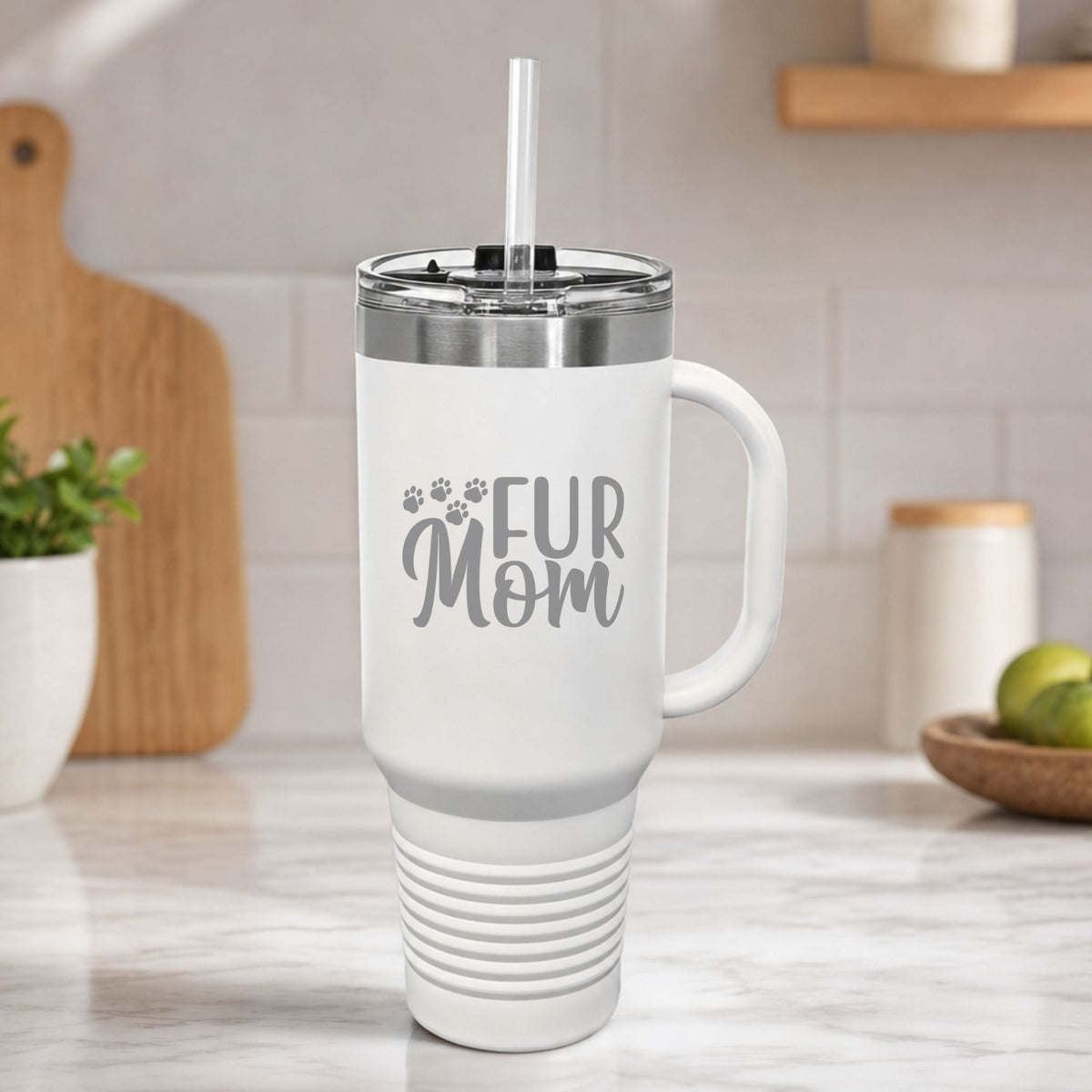 White 40 oz tumbler with handle and straw laser engraved with "Fur Mom", plus paw prints, on a kitchen counter