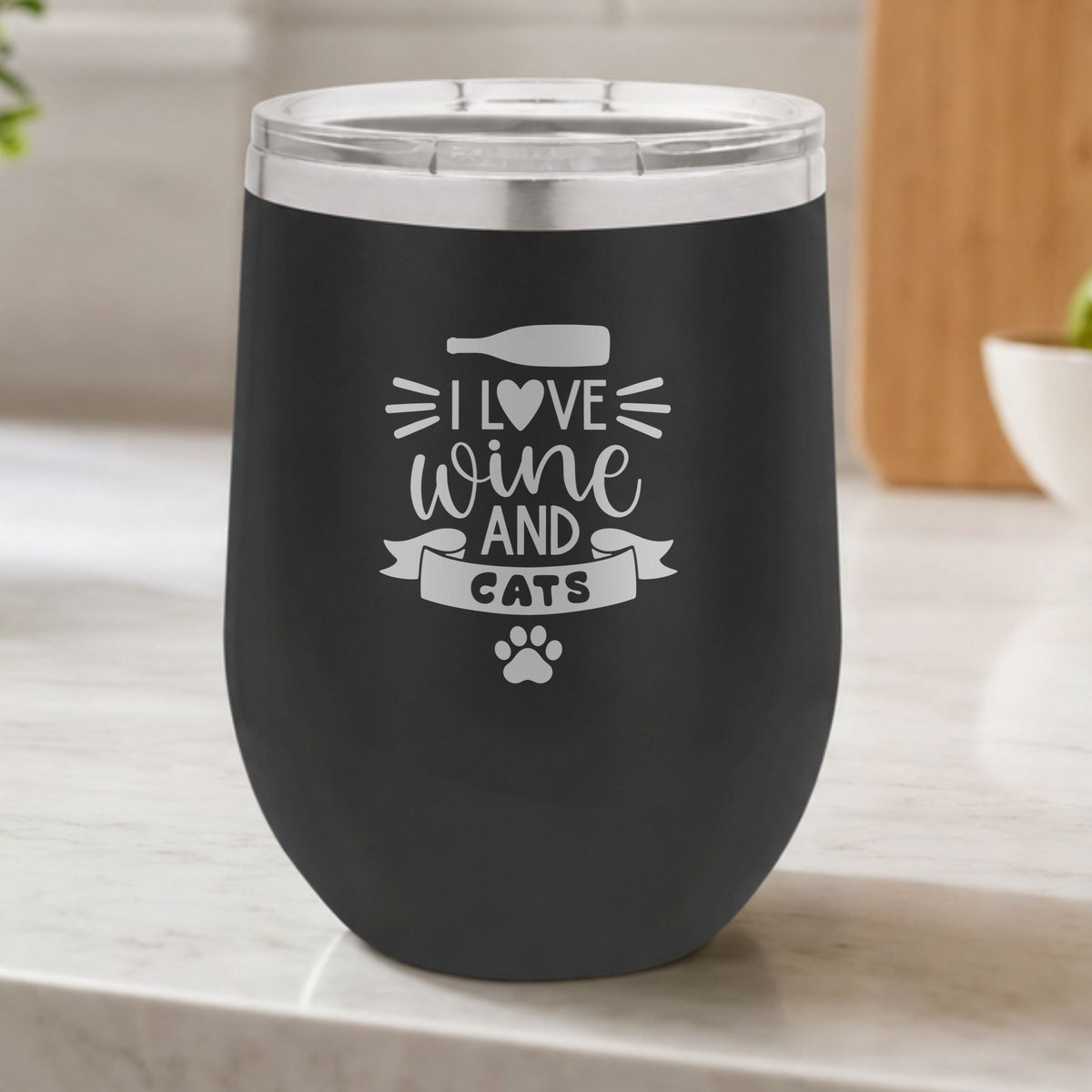 Black 12 oz stemless wine tumbler laser engraved with "I Love Wine and Cats", a wine bottle, a heart and a paw print, on a kitchen counter