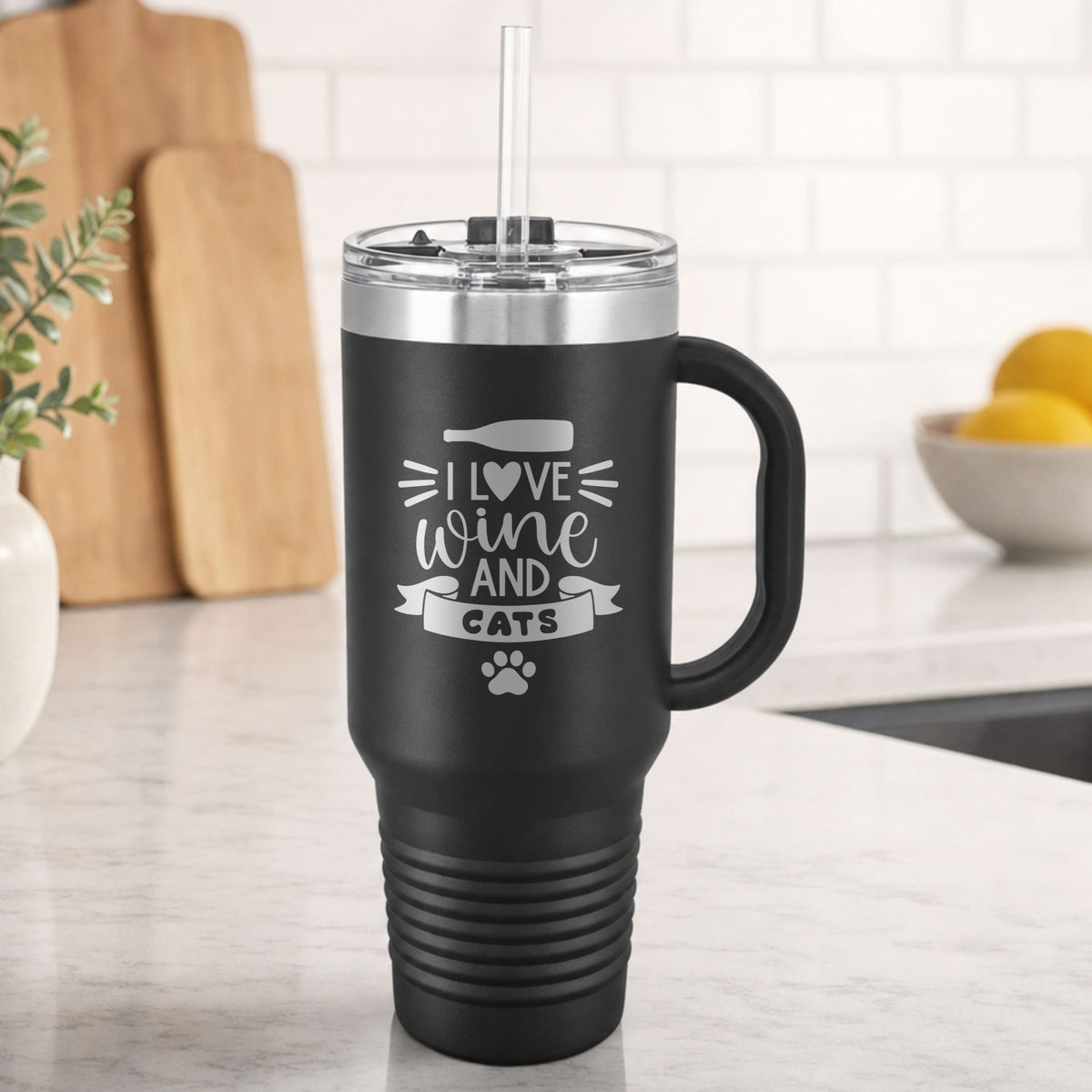 Black 40 oz tumbler with handle and straw laser engraved with "I Love Wine and Cats", a wine bottle, a heart and a paw print, on a kitchen counter