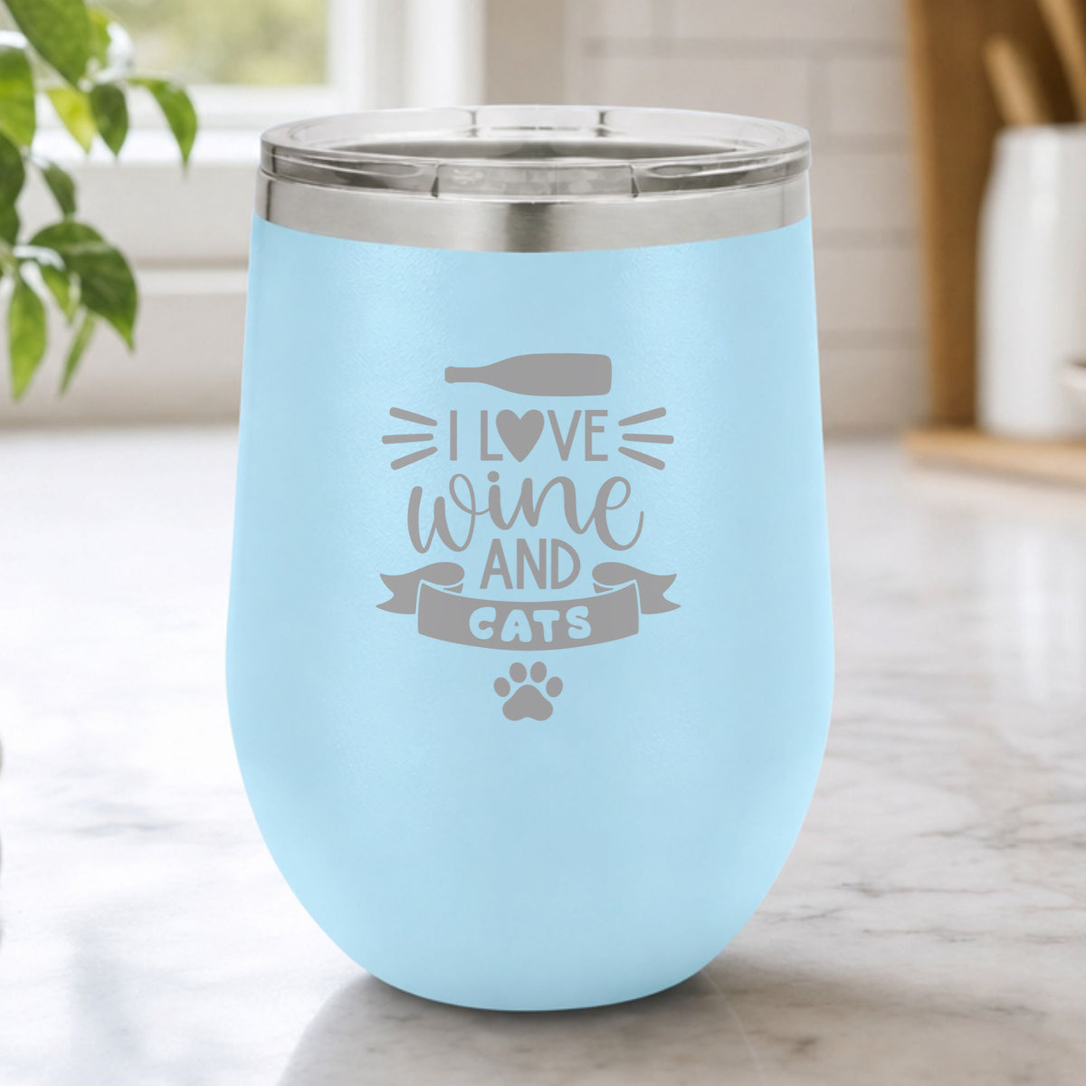 Light Blue 12 oz stemless wine tumbler laser engraved with "I Love Wine and Cats", a wine bottle, a heart and a paw print, on a kitchen counter