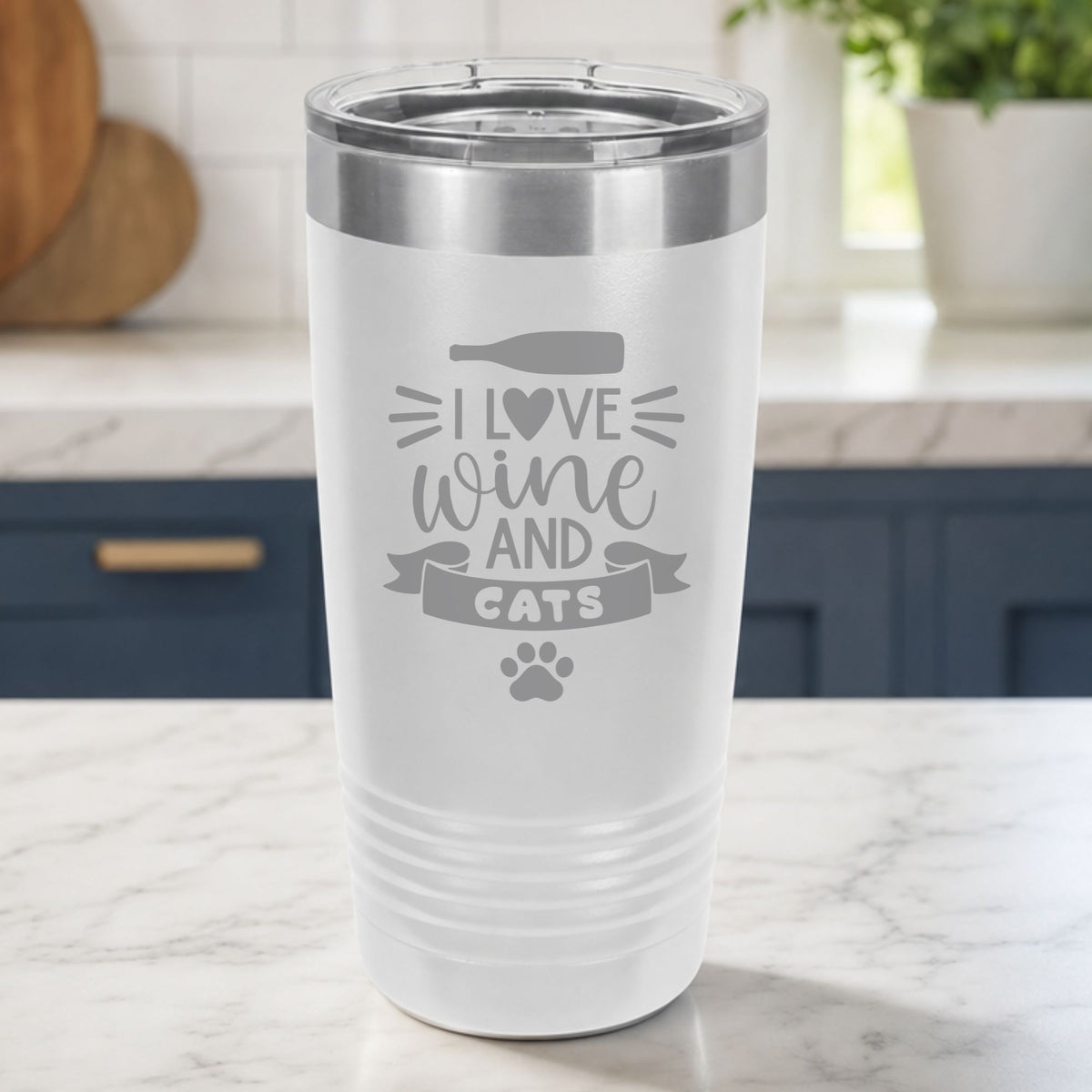 White 20 oz tumbler laser engraved with "I Love Wine and Cats", a wine bottle, a heart and a paw print, on a kitchen counter