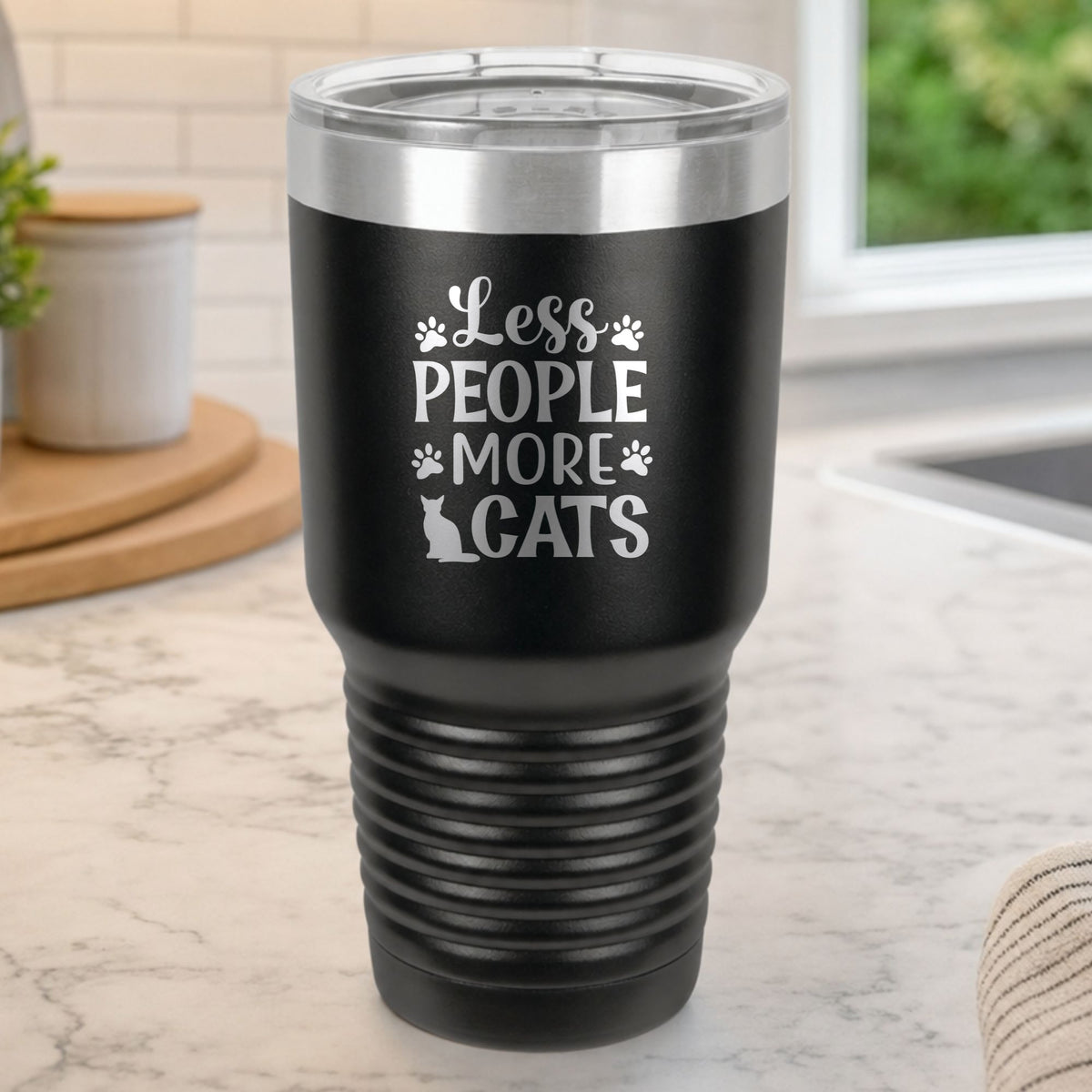 Black 30 oz tumbler laser engraved with "Less People, More Cats", plus paw prints and a sitting cat, on a kitchen counter