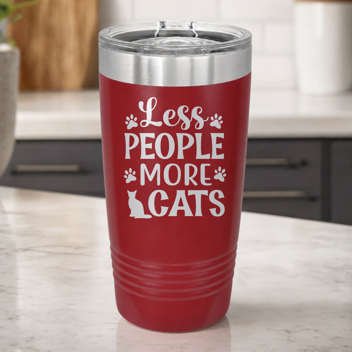 Maroon 20 oz tumbler laser engraved with "Less People, More Cats", plus paw prints and a sitting cat, on a kitchen counter
