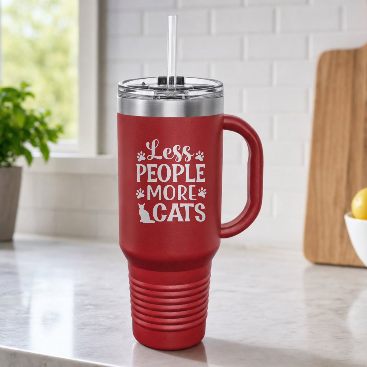 Maroon 40 oz tumbler with handle and straw laser engraved with "Less People, More Cats", plus paw prints and a sitting cat, on a kitchen counter