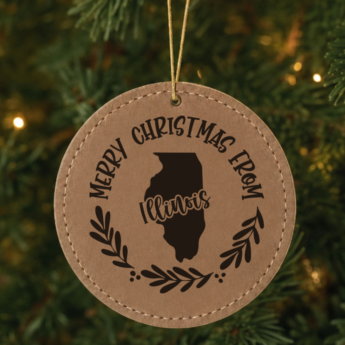 Brown leatherette round Christmas ornament engraved Merry Christmas From Illinois, with the state shape in a laurel wreath, hanging on a tree