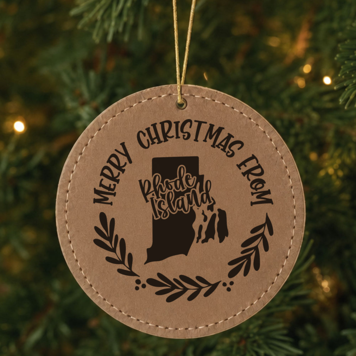 Brown leatherette round Christmas ornament engraved Merry Christmas From Rhode Island, with the state shape in a laurel wreath, hanging on a tree