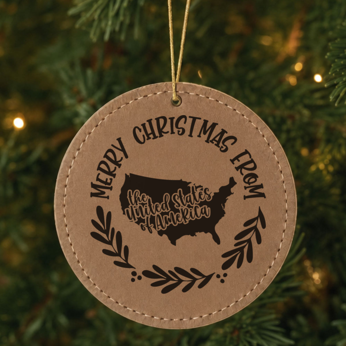 Brown leatherette round Christmas ornament engraved Merry Christmas From the USA, with the country shape in a laurel wreath, hanging on a tree