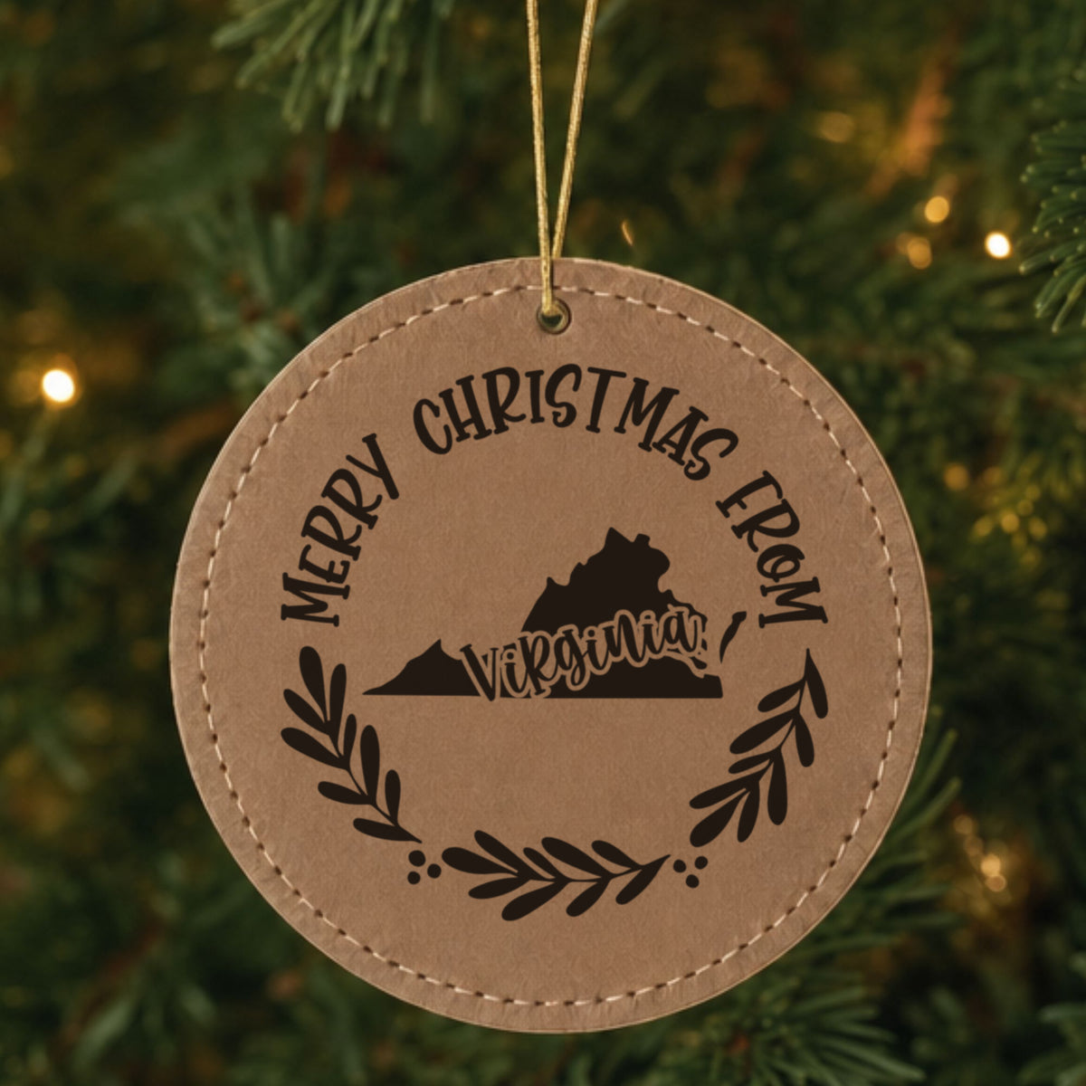 Brown leatherette round Christmas ornament engraved Merry Christmas From Virginia, with the state shape in a laurel wreath, hanging on a tree