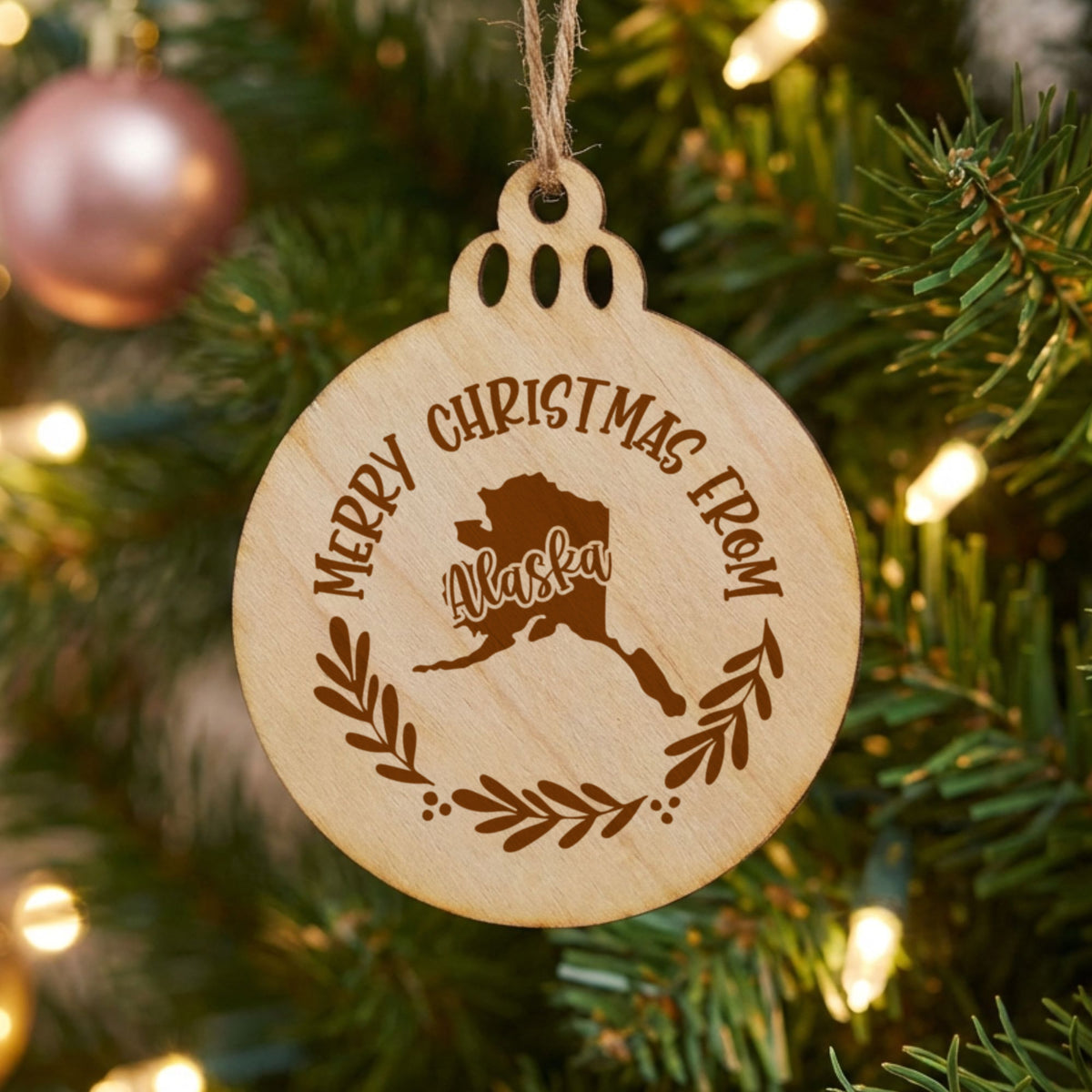 Round wood Christmas ornament engraved Merry Christmas From Alaska, with the state shape in a laurel wreath