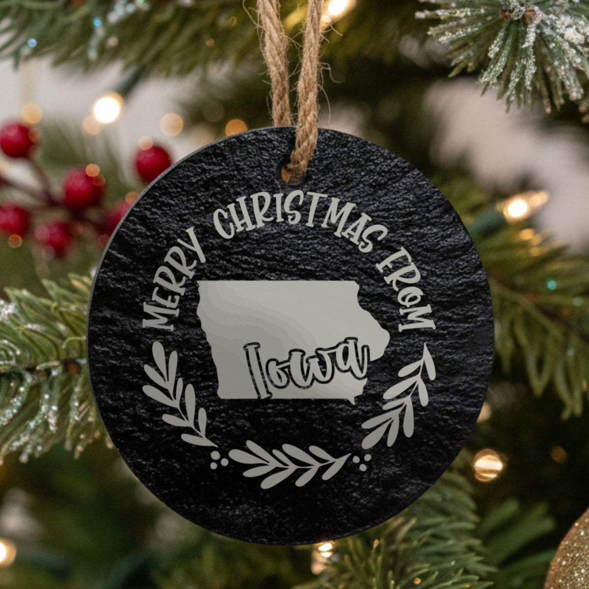 Round slate Christmas ornament engraved Merry Christmas From Iowa, with the state shape in a laurel wreath