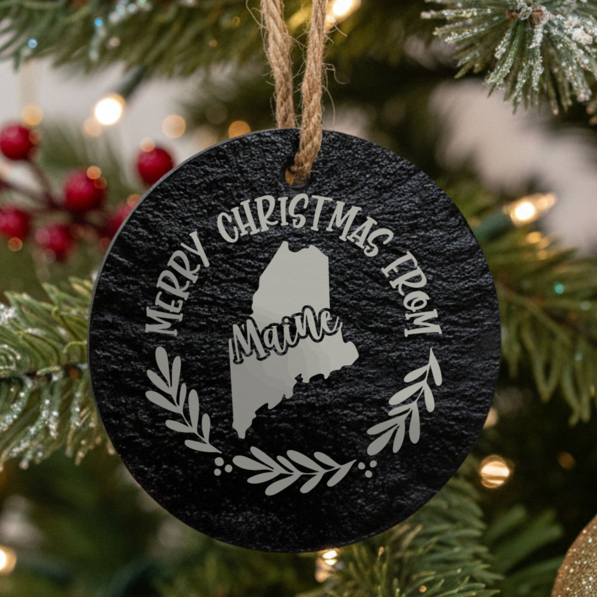 Round slate Christmas ornament engraved Merry Christmas From Maine, with the state shape in a laurel wreath