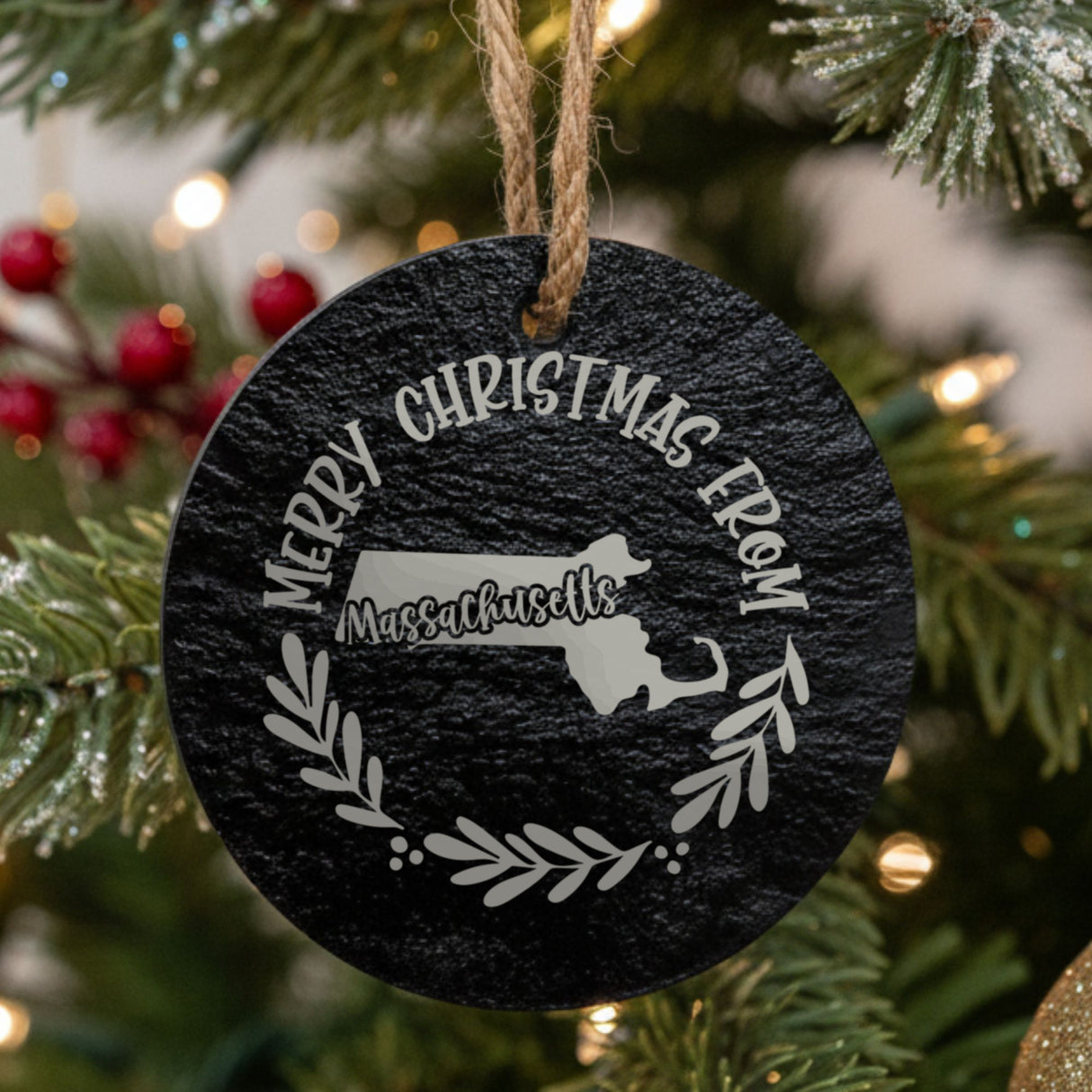 Round slate Christmas ornament engraved Merry Christmas From Massachusetts, with the state shape in a laurel wreath