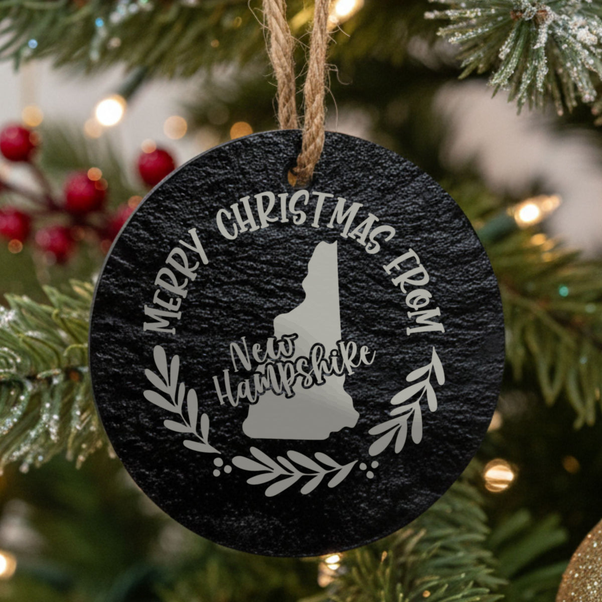 Round slate Christmas ornament engraved Merry Christmas From New Hampshire, with the state shape in a laurel wreath