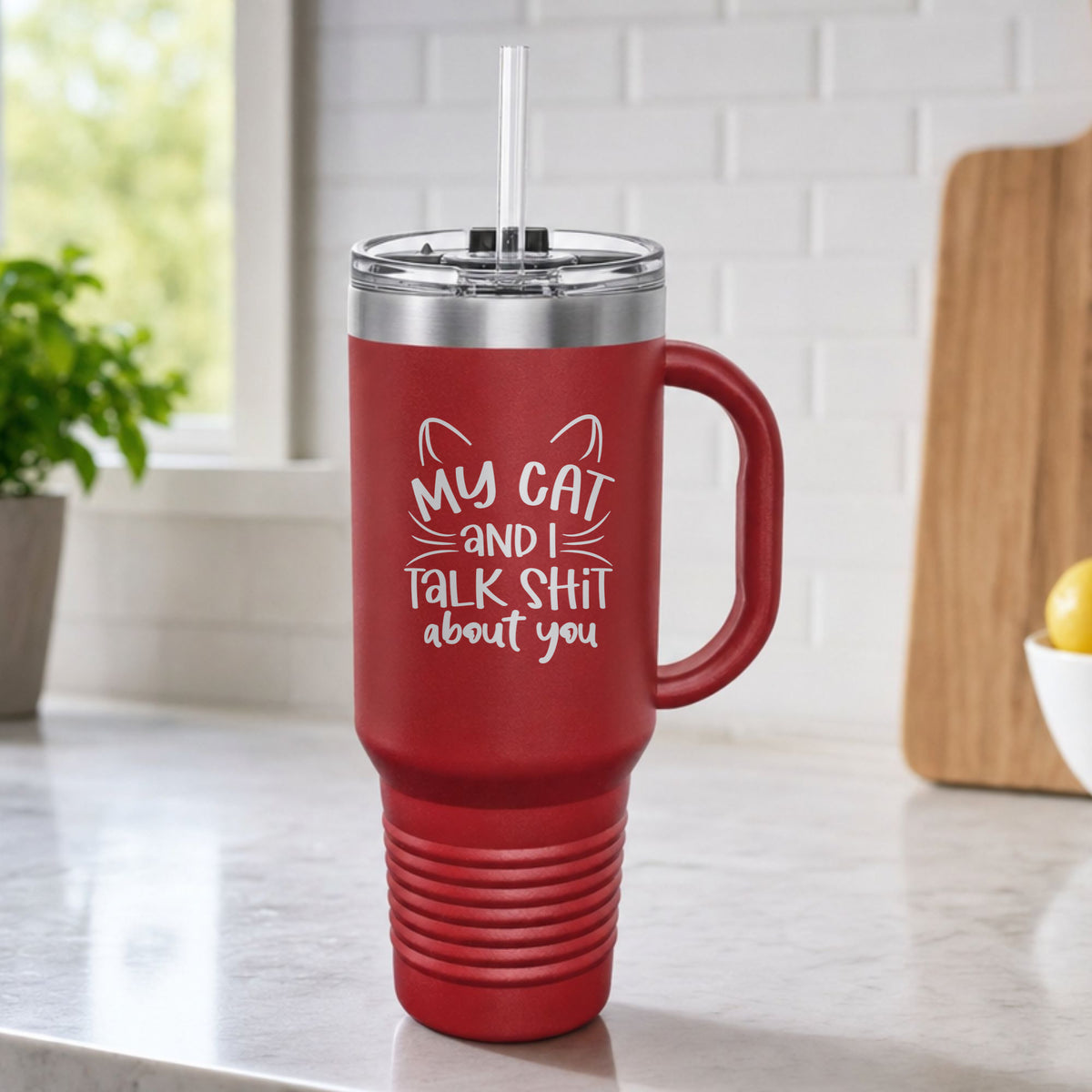 Maroon 40 oz tumbler with handle and straw laser engraved with "My Cat and I Talk Sh*t About You", plus cat ears and whiskers, on a kitchen counter