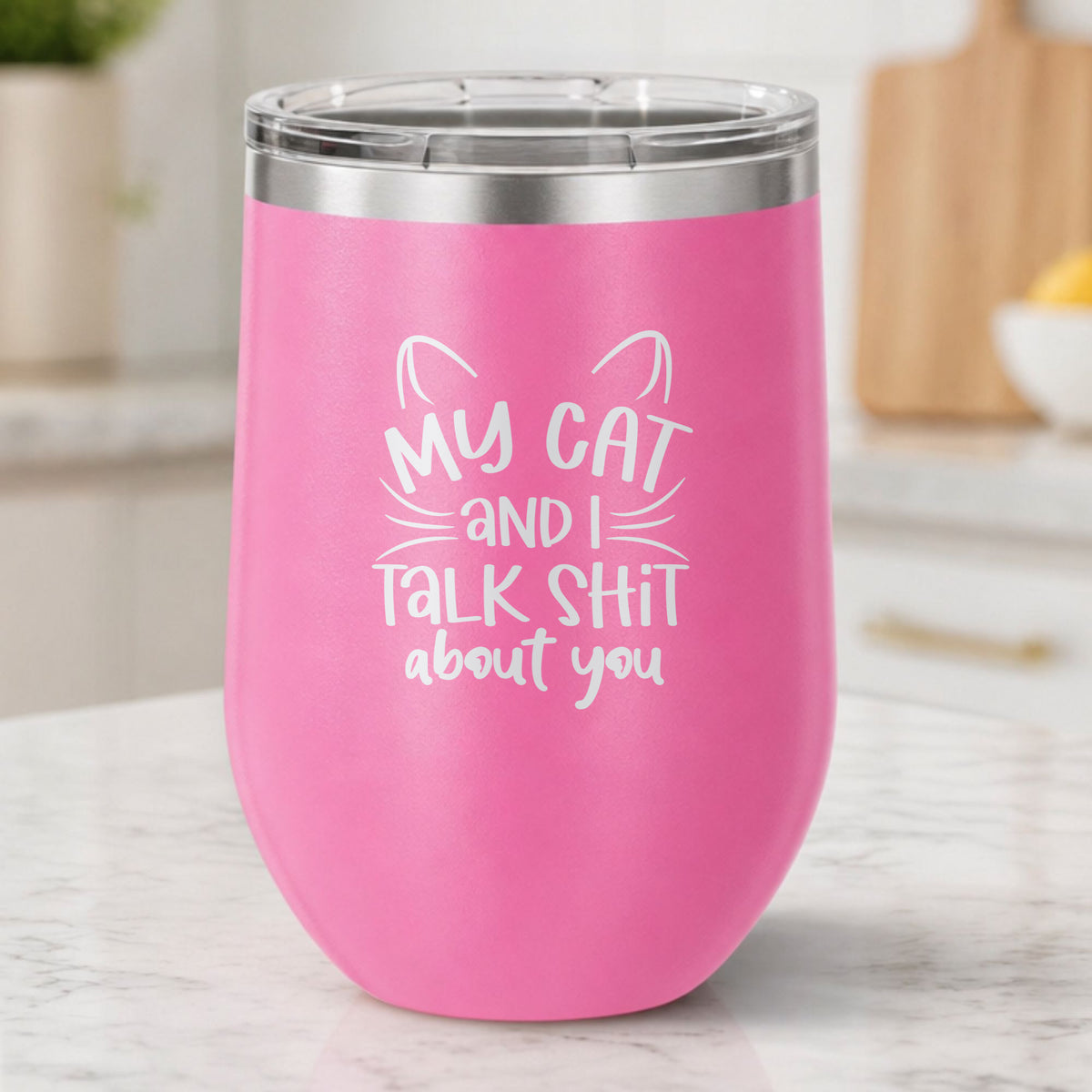 Pink 12 oz stemless wine tumbler laser engraved with "My Cat and I Talk Sh*t About You", plus cat ears and whiskers, on a kitchen counter