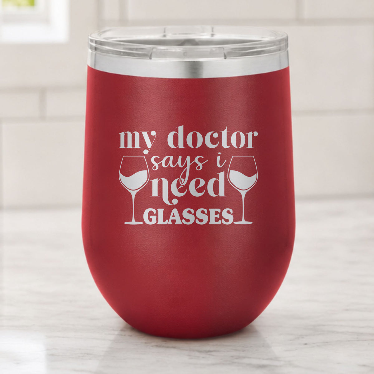 Maroon 12 oz stemless wine tumbler laser engraved with "My Doctor Says I Need Glasses", on a kitchen counter