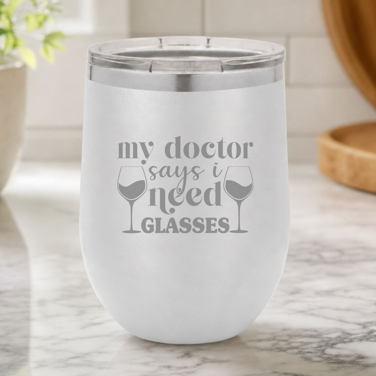 White 12 oz stemless wine tumbler laser engraved with "My Doctor Says I Need Glasses", on a kitchen counter