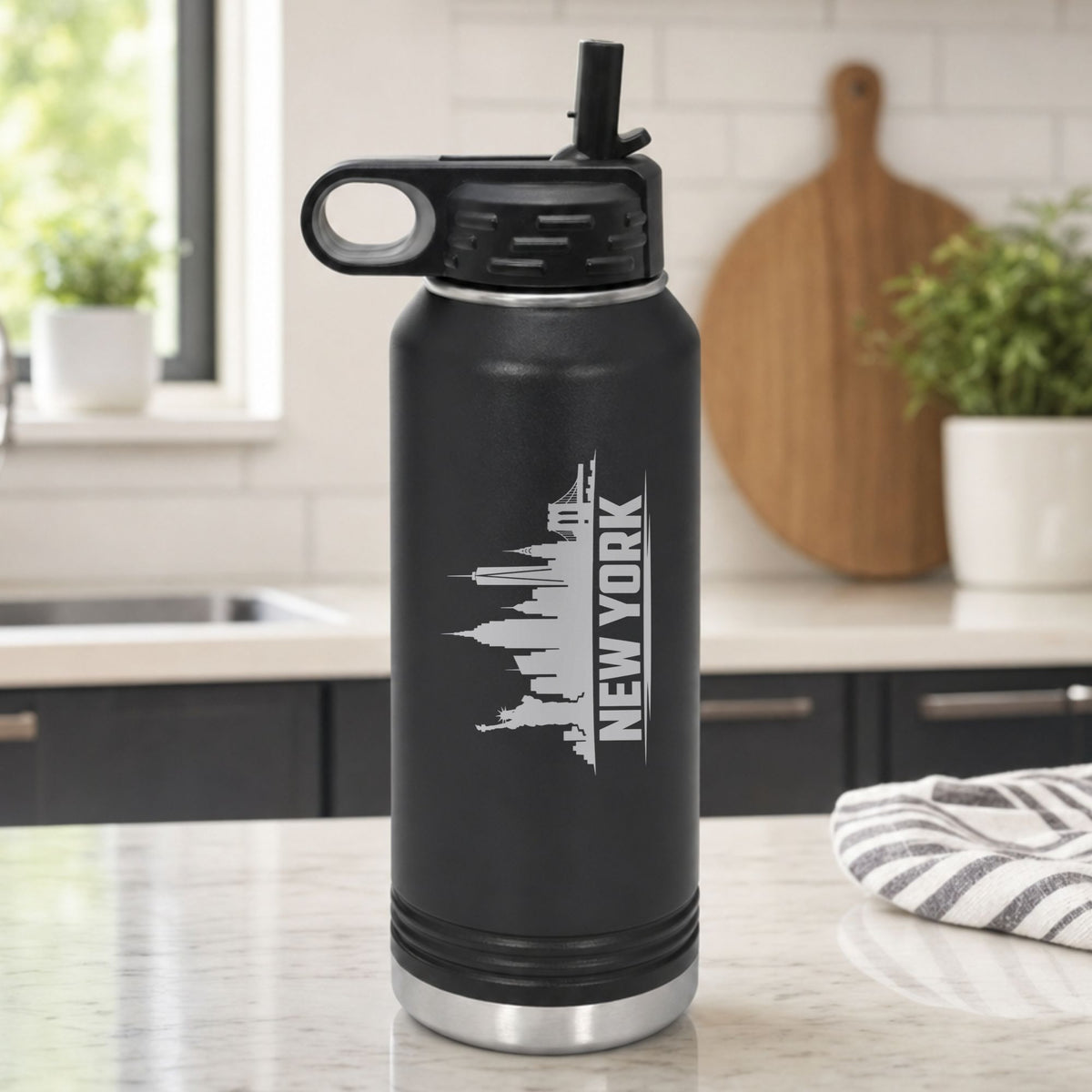 Black 32 oz insulated water bottle laser engraved with the New York, New York skyline running up the side, standing on a kitchen counter